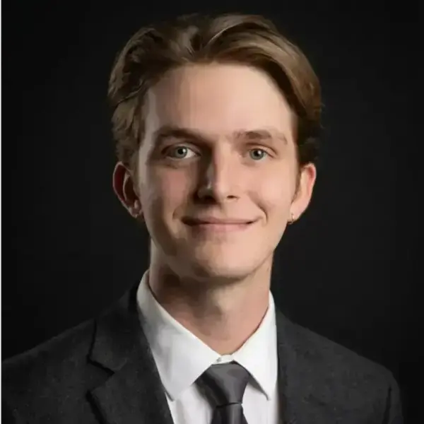 Headshot of Decker Pope. He is a white male with brown hair, wearing a white collared shirt, black tie, and back suit jacket.